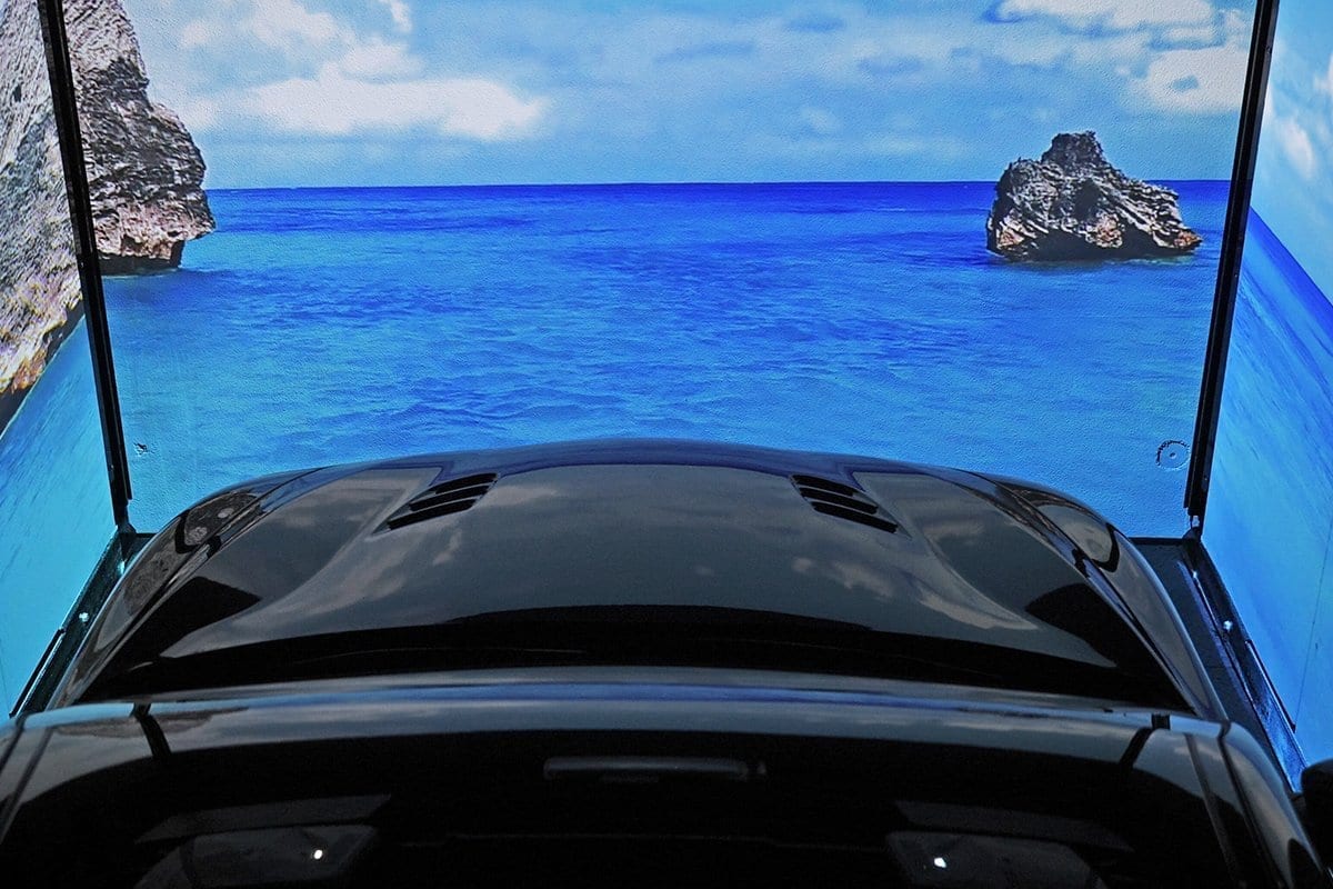 Coche negro visto desde el interior con techo panorámico abierto, vista del mar azul con rocas y cielo azul