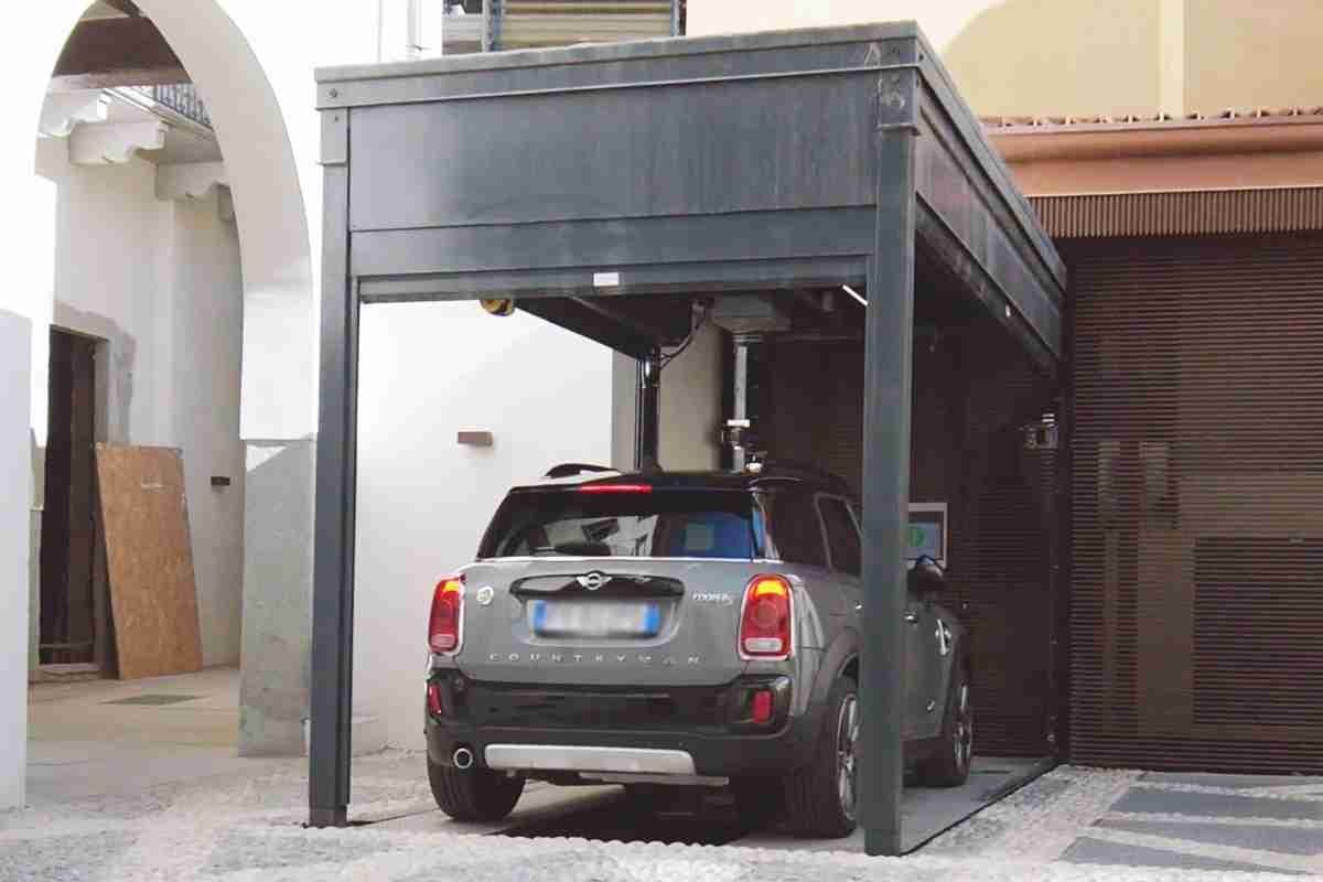 Coche gris aparcado bajo estructura metálica gris con techo, patio interior con edificios residenciales
