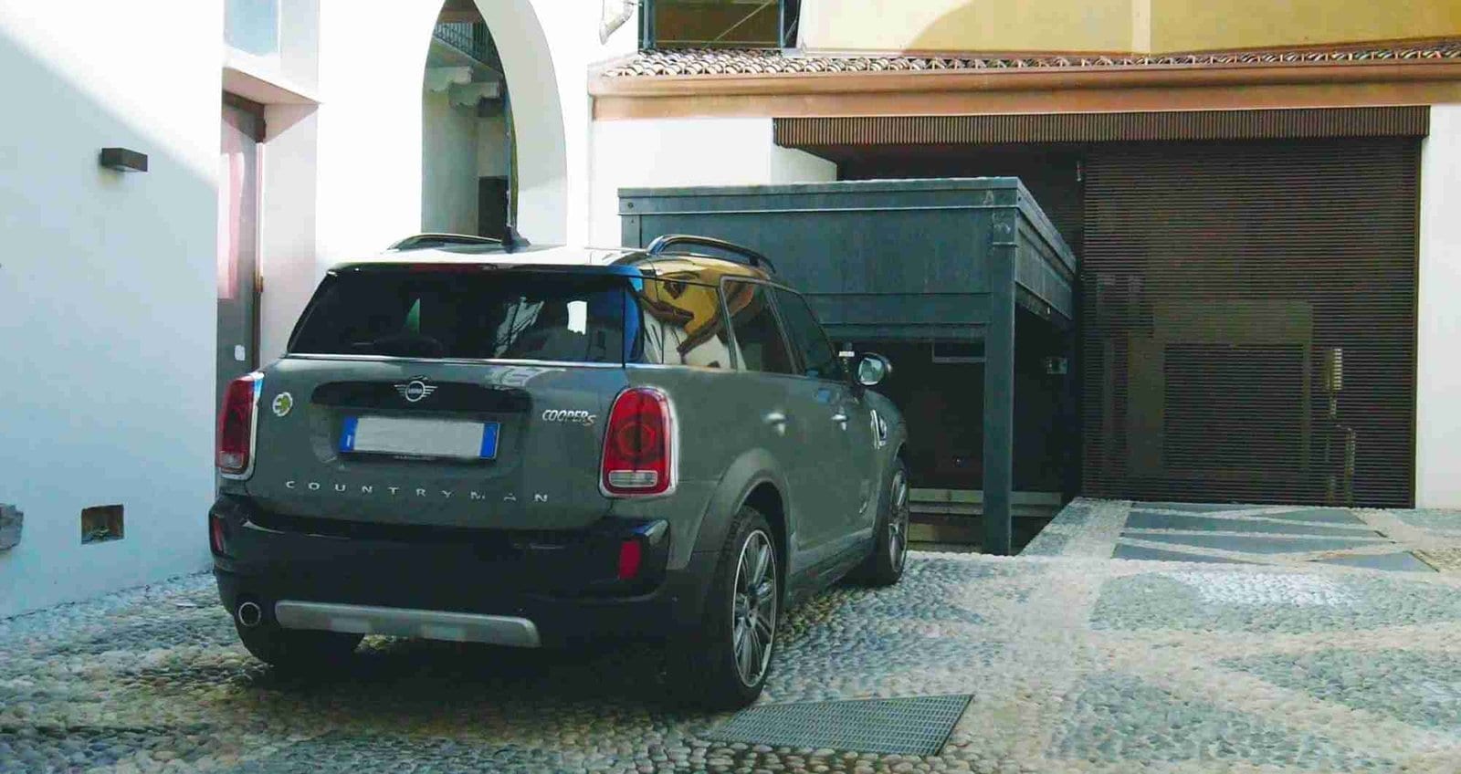 Coche verde aparcado frente a estructura metálica verde, patio con edificios residenciales al fondo