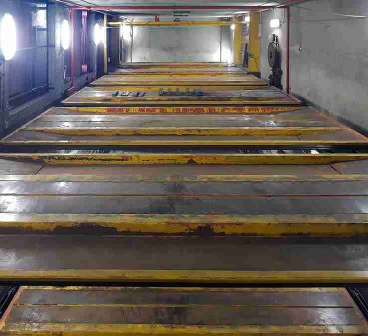 Interior del aparcamiento automático antes de la renovación - plataformas amarillas y rojas oxidadas, paredes sucias, iluminación deficiente
